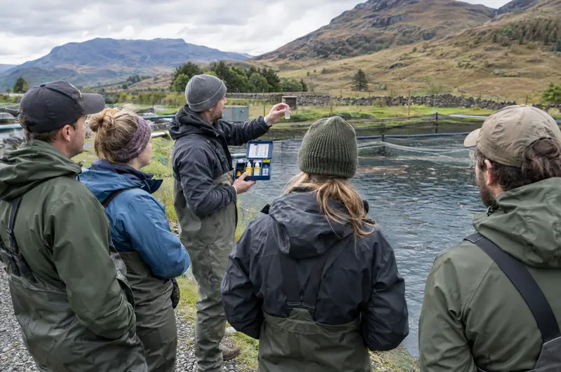Group of adults learning water testing beside a trout farm pond